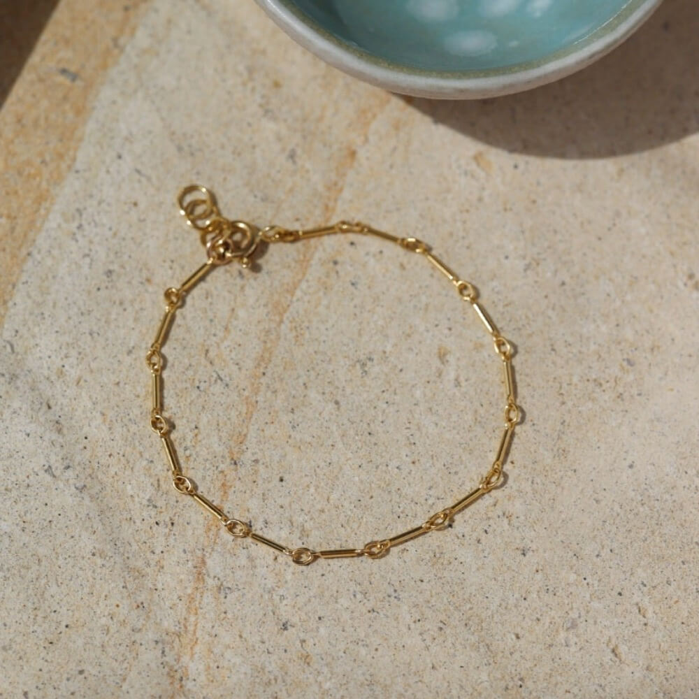 Gold bar link chain, displayed on a stone backdrop. 