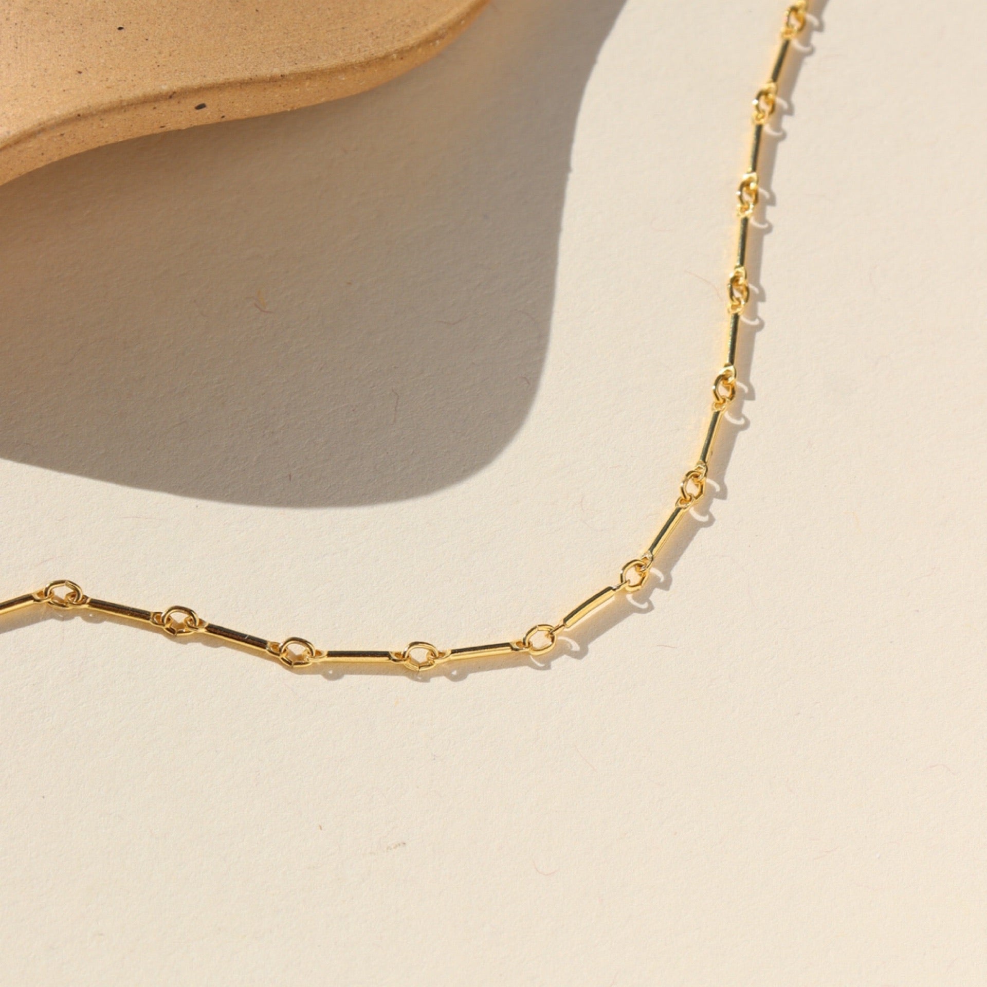 Bar and Link 14k gold fill chain close up laid on a beige background in the sunlight 