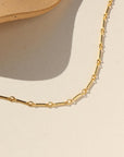 Gold bar link chain, displayed on a cream backdrop. 