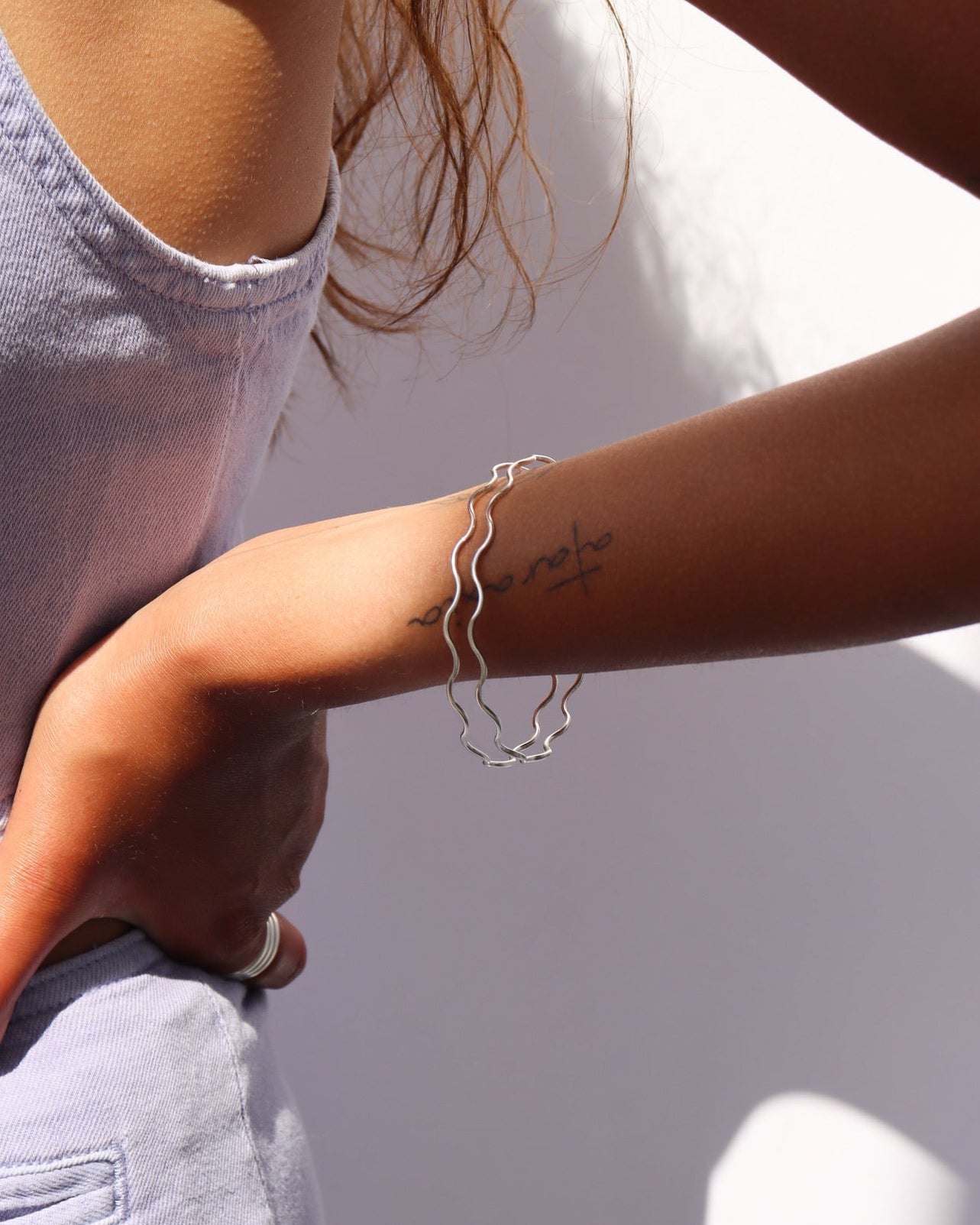 Model wearing two sterling silver bangles with wave-like textured wire
