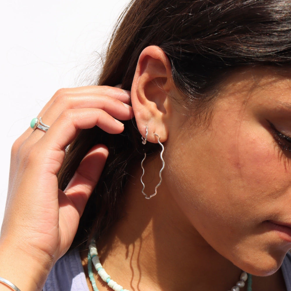 Model wearing a sterling silver hoop with wave-like textured wire, model paired it with a huggie with the same textured pattern
