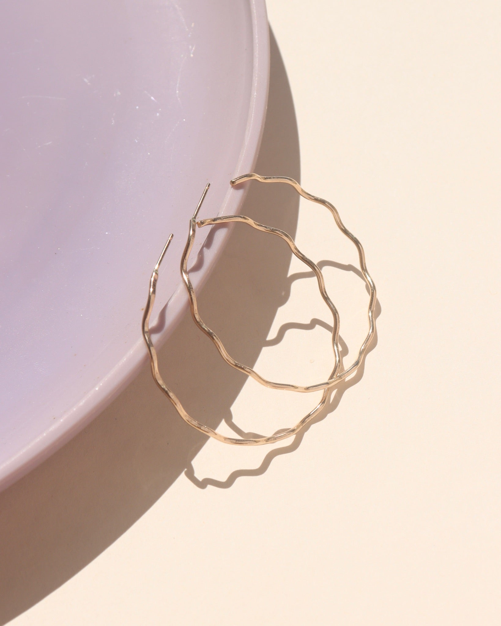 14k gold fill hoop with wave-like textured wire, displayed on a cream backdrop in natural sunlight