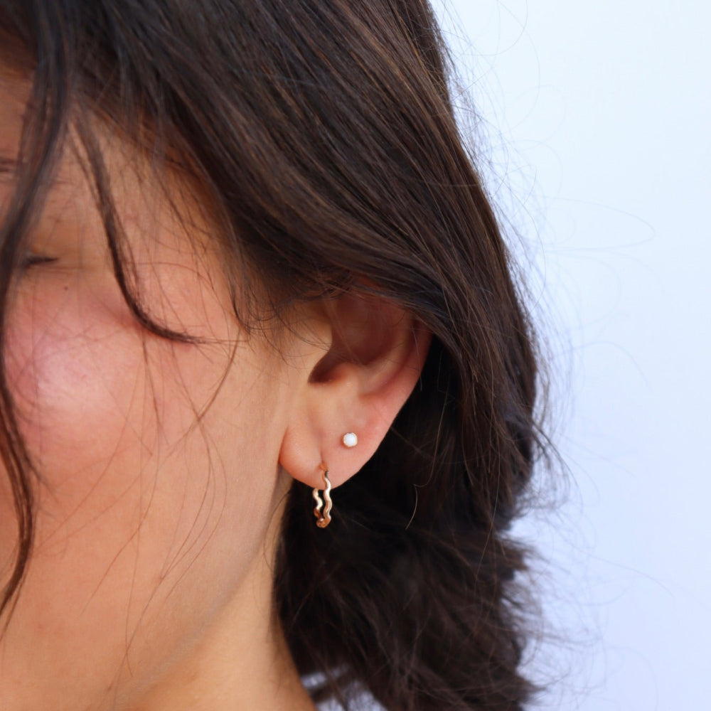 Model wearing a wave like 14k gold fill textured huggie earring.