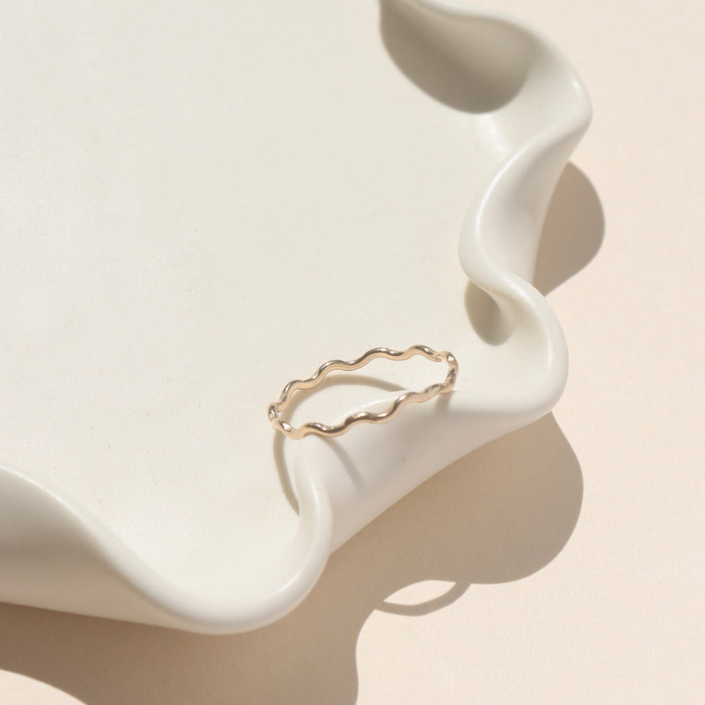 14k gold fill ring with wave-like textured wire, displayed on a cream dish in natural sunlight