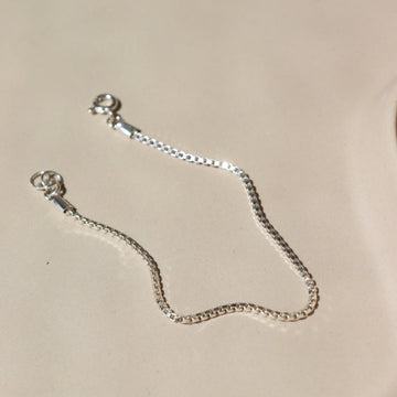 925 sterling silver Delaney anklet laid on a tan paper in the sunlight.