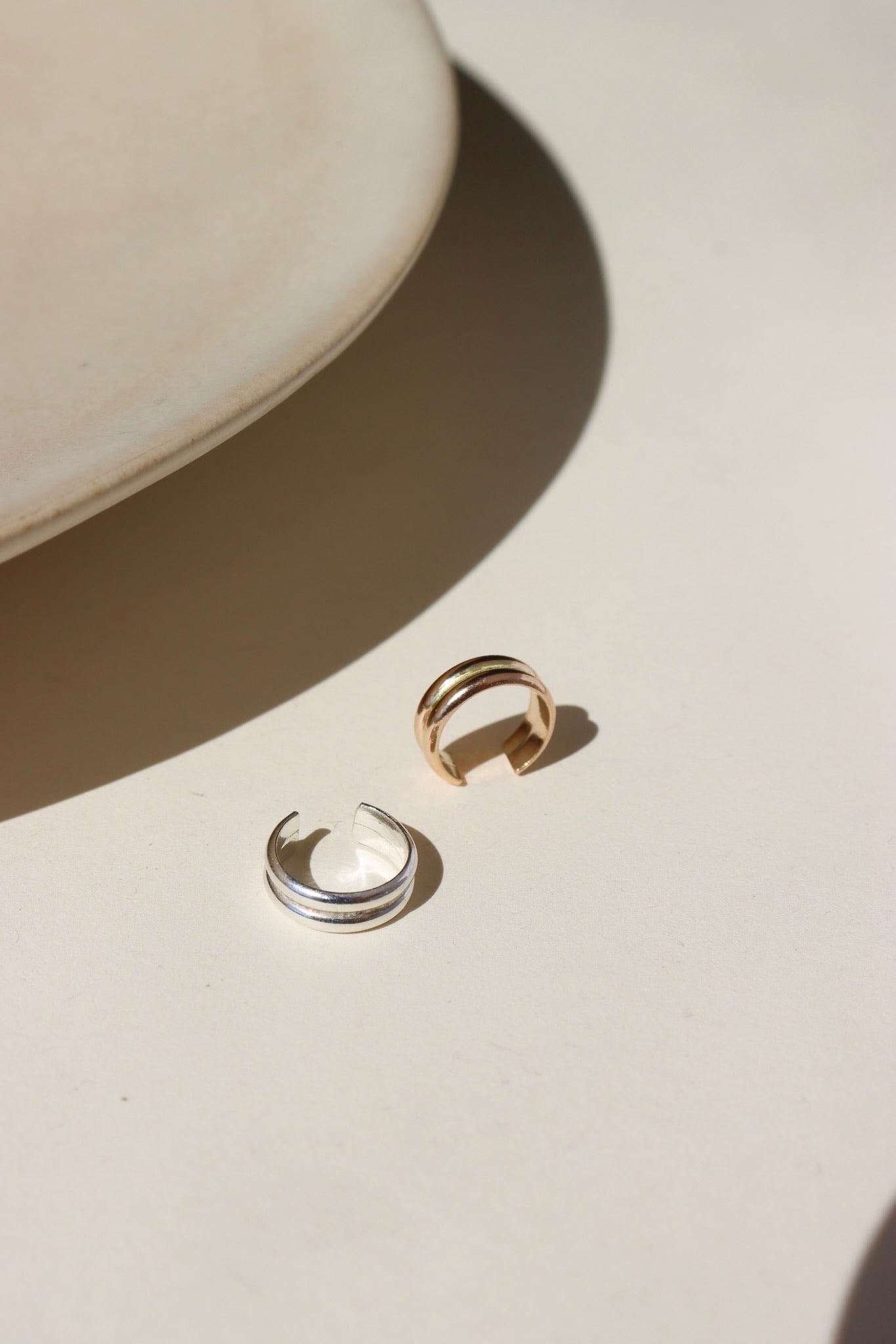 A 14k gold fill + sterling silver doubled layered ear cuff, displayed on a cream backdrop in the sunlight 