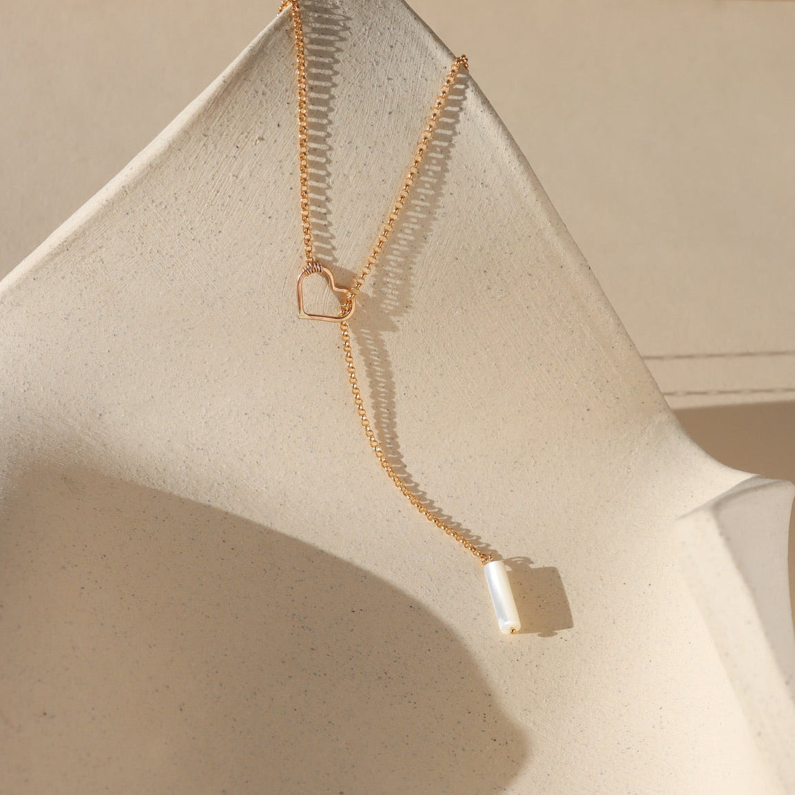 14k gold fill lariat necklace with heart component and mother of pearl bead in the sunlight