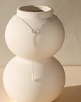 sterling silver lariat necklace with mother of pearl bead displayed on a vase