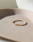 14k gold fill ring placed on a peach colored plate. The plate and ring is placed in the sunlight. This ring features a lightly hammered gold stacking ring, handmade by Token Jewelry in Eau Claire, Wisconsin