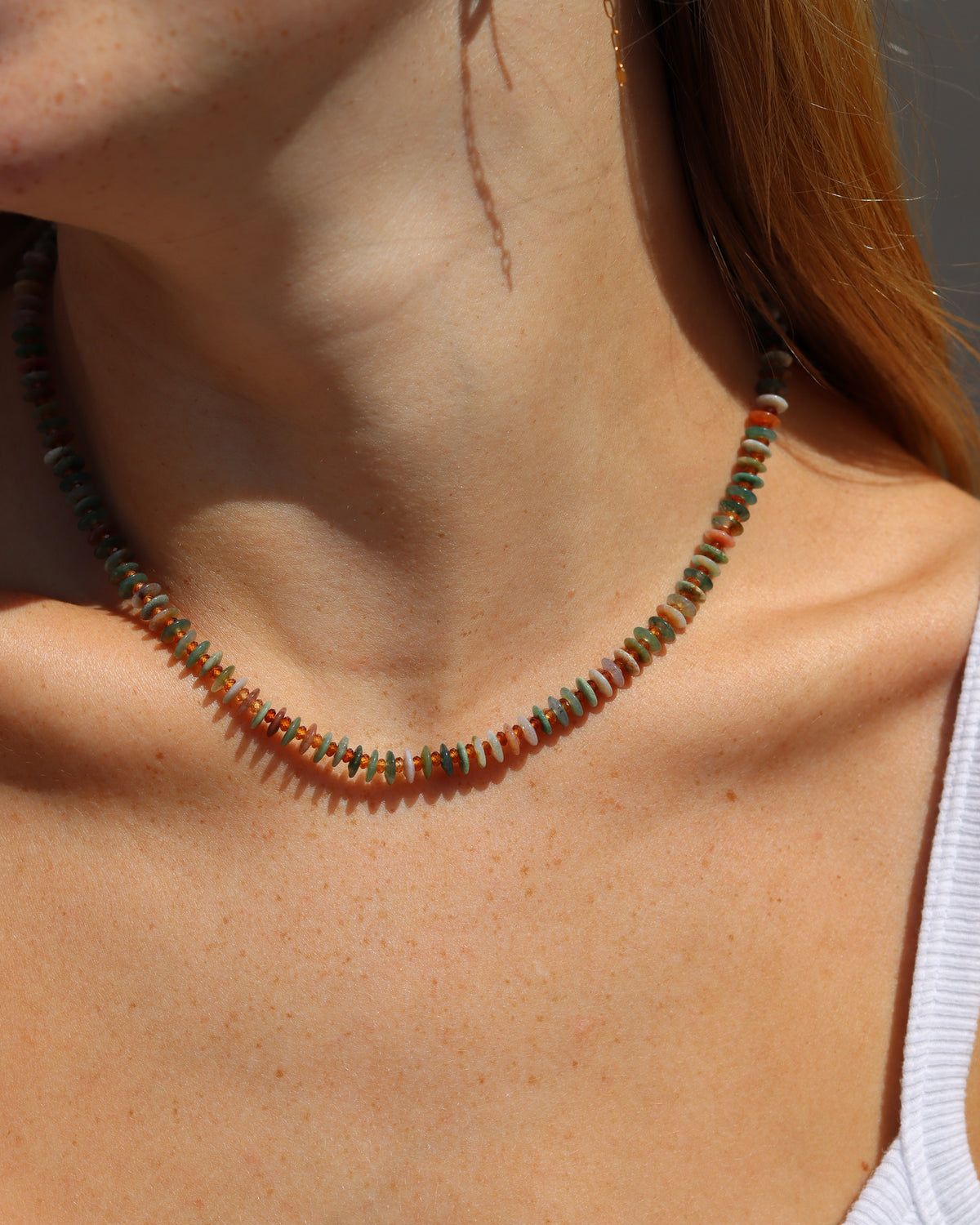 Multicolored gemstone disc bead necklace in soft green, turquoise, blush, and amber tones, worn in warm sunlight.
