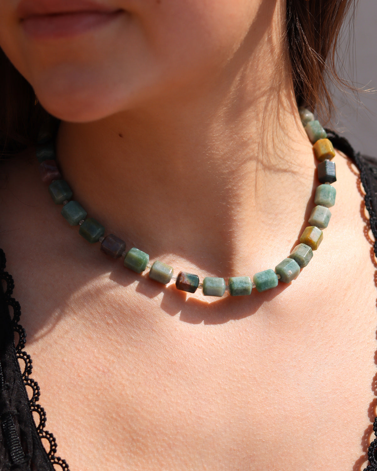Chunky multicolored stone bead necklace in turquoise, green, blue, and earthy tones, worn with a black top in warm sunlight.