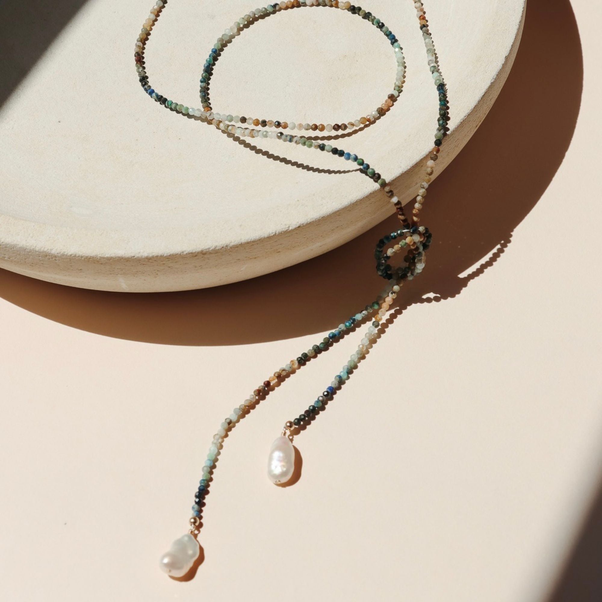 beaded wrap necklace with large pearls on a light dish