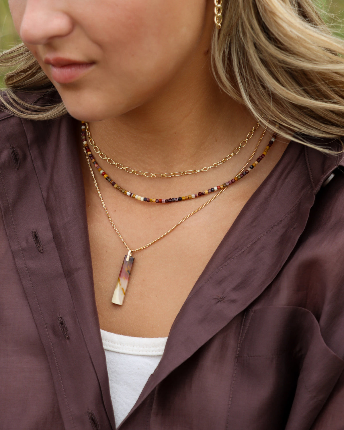 Model wearing a multicolored gemstone beaded necklace layered with delicate gold chains and a rectangular gemstone pendant.