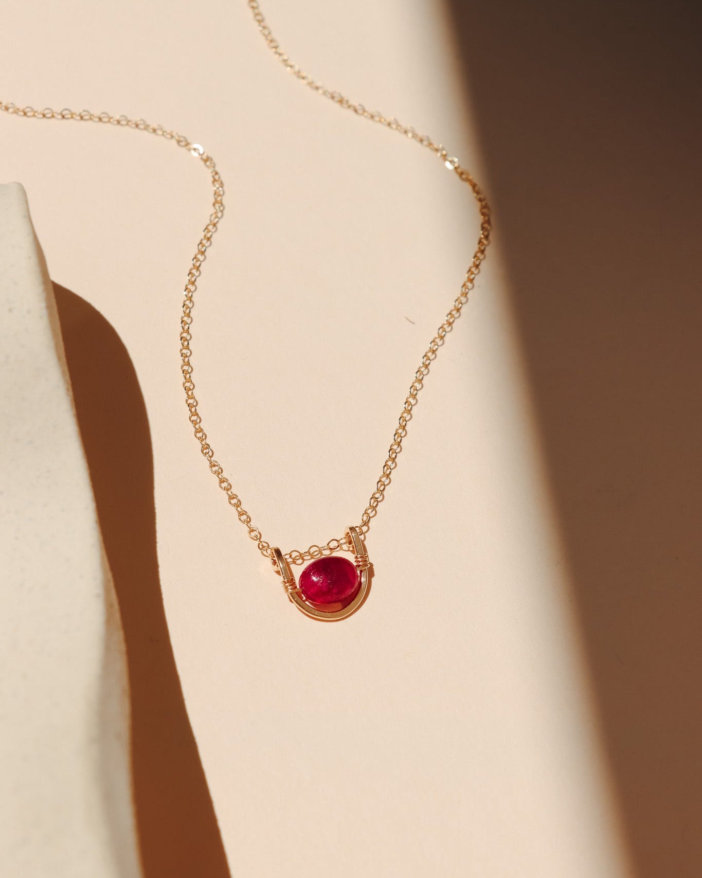 14k gold fill chain necklace with ruby and wire pendant on a light surface