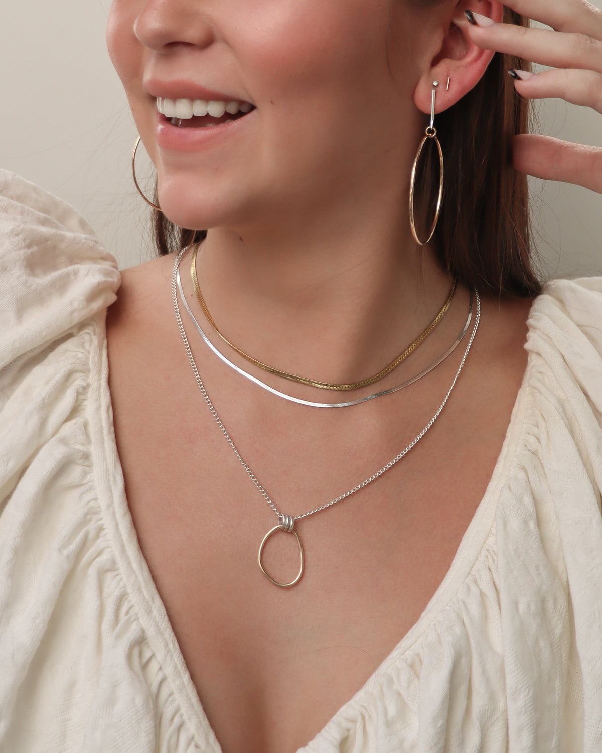 Model wearing the Forma mixed metal pendant necklace with a gold fill oval pendant and sterling silver chain, layered with gold and silver necklaces and paired with mixed metal Earrings.