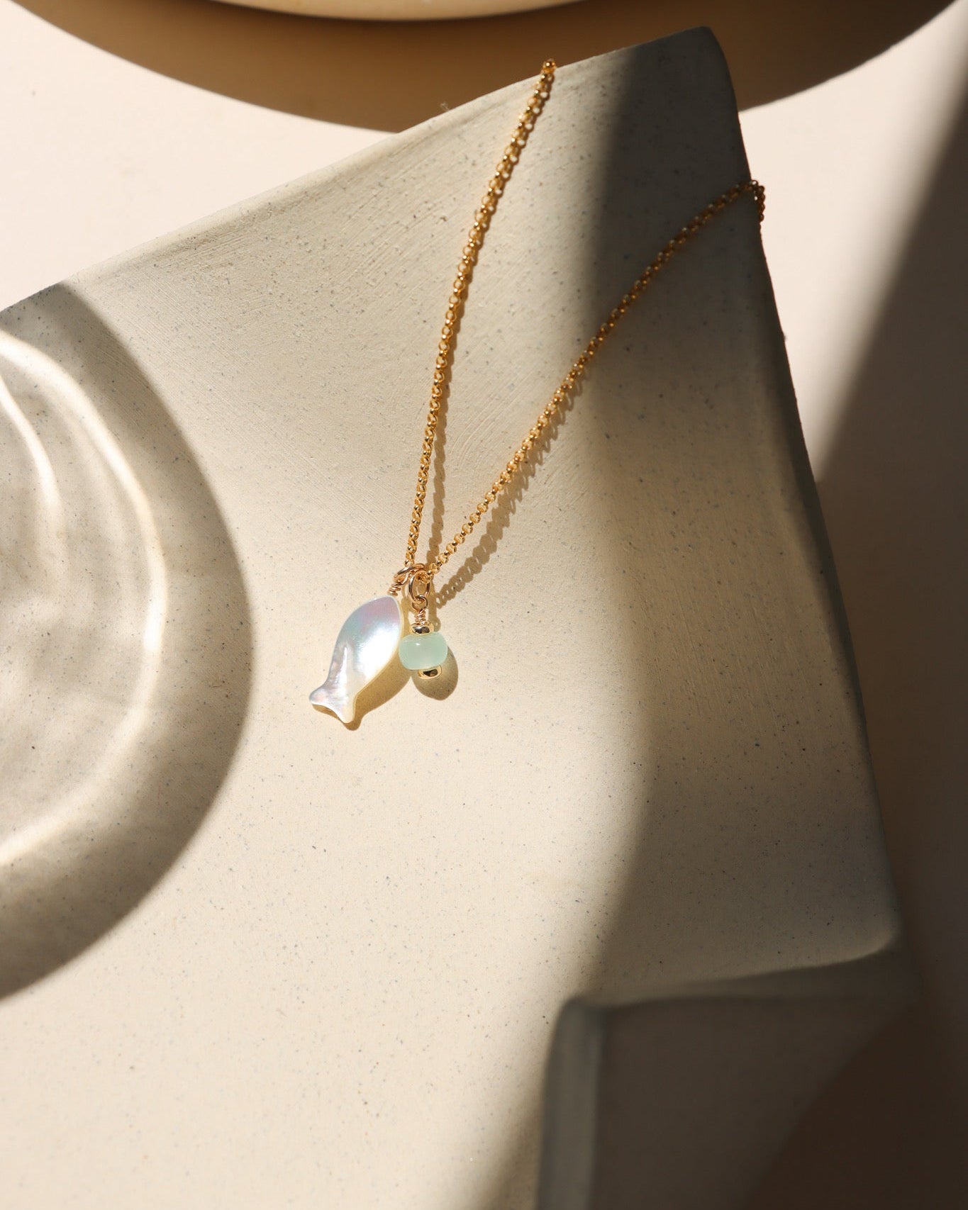 14k gold fill rolo chain necklace with mother of pearl fish and opal charms on a light dish