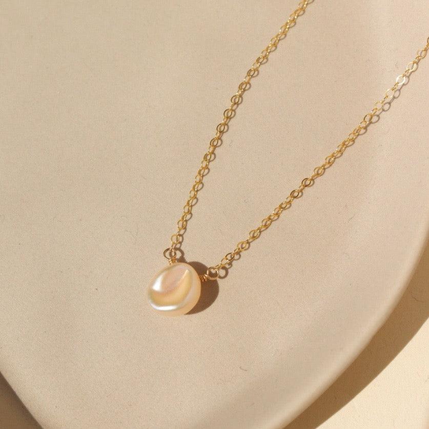 14k gold fill freshwater pearl necklace laid on a peach colored plate. This necklace features the simple chain with the freshwater pearl wired in the middle.