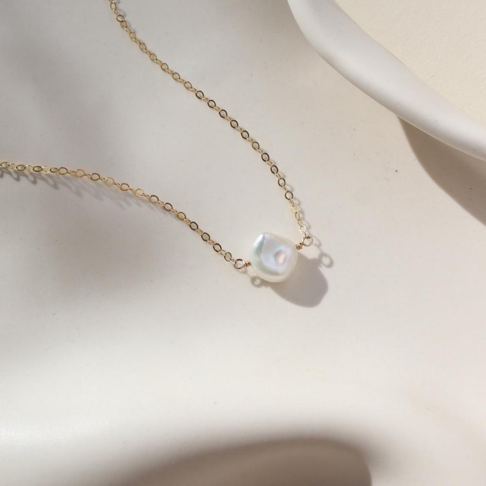 14k gold filled Freshwater Pearl Necklace resting on a white dish. This necklace features the simple chain with the freshwater pearl  wired in the middle.