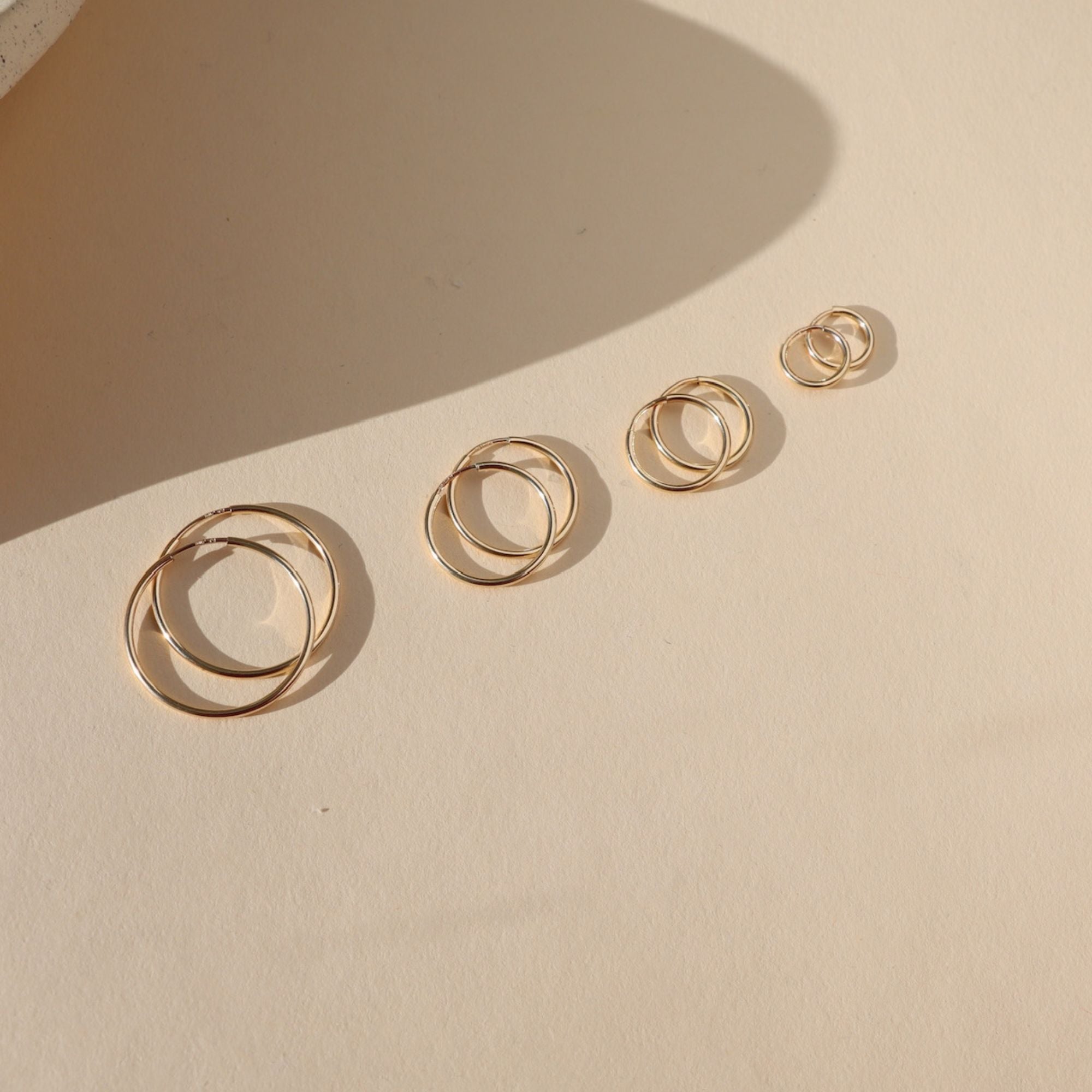 Product photo of Goldie Hoops, 14k gold fill endless hoop earrings in four graduated sizes, displayed on a light surface in warm natural sunlight.