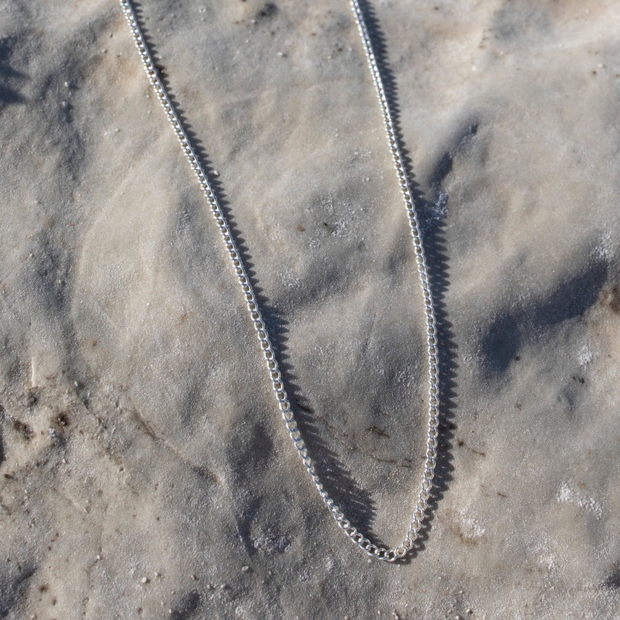 925 sterling silver la mer necklace laid on the beach in the sand.