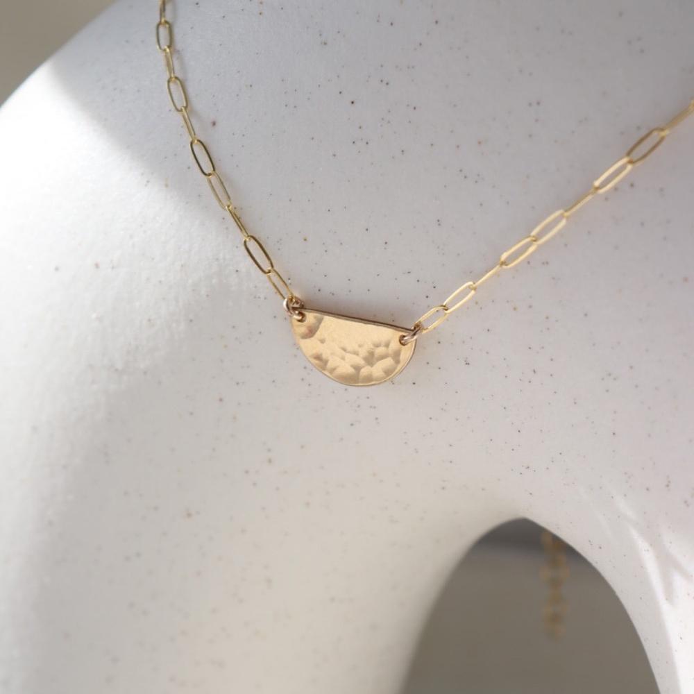 14k gold fill necklace Laid on a white pot. This necklace features a half circle hammered in the middle each side connected by the cosset chain.