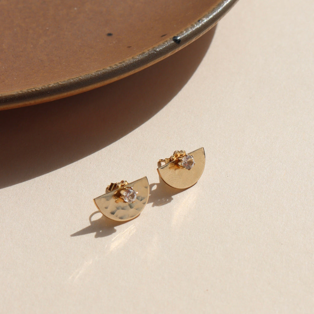 14k gold fill hammered metal ear jackets in a half moon shape, paired with April birthstone studs, displayed on a cream backdrop in the sunlight 