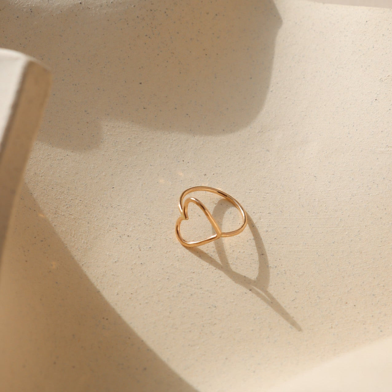 Gold heart-shaped ring on a textured beige surface