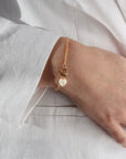 Model wearing the mother of pearl toggle bracelet. This bracelet features a gold curb chain with a toggle clasp opening with a mother of pearl heart at the end. 