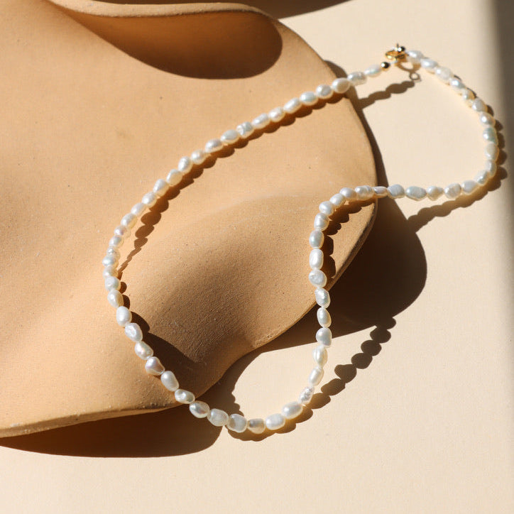 handmade pearl beaded necklace with 14k gold fill clasp on a light dish