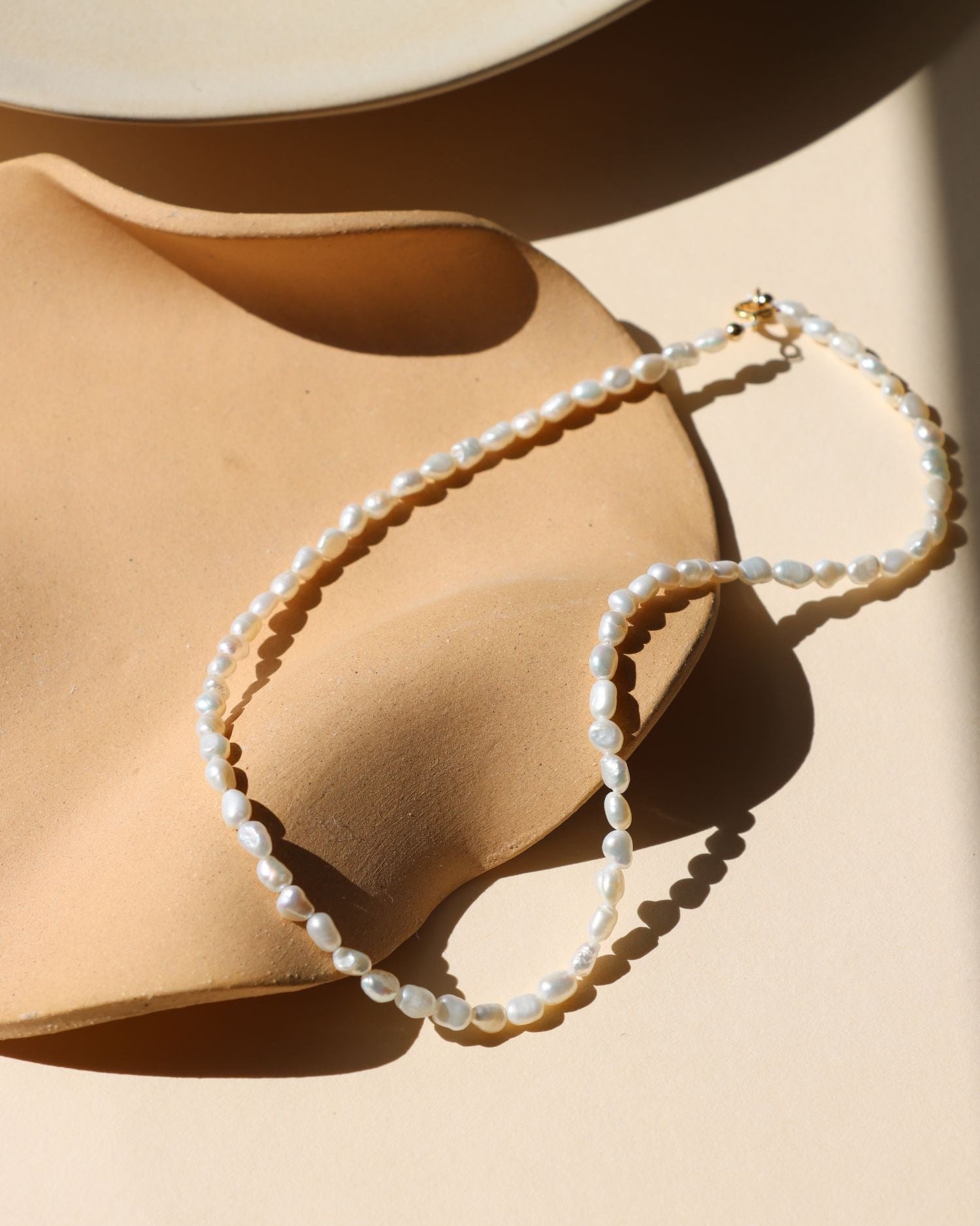 handmade pearl beaded necklace with 14k gold fill clasp on a light dish