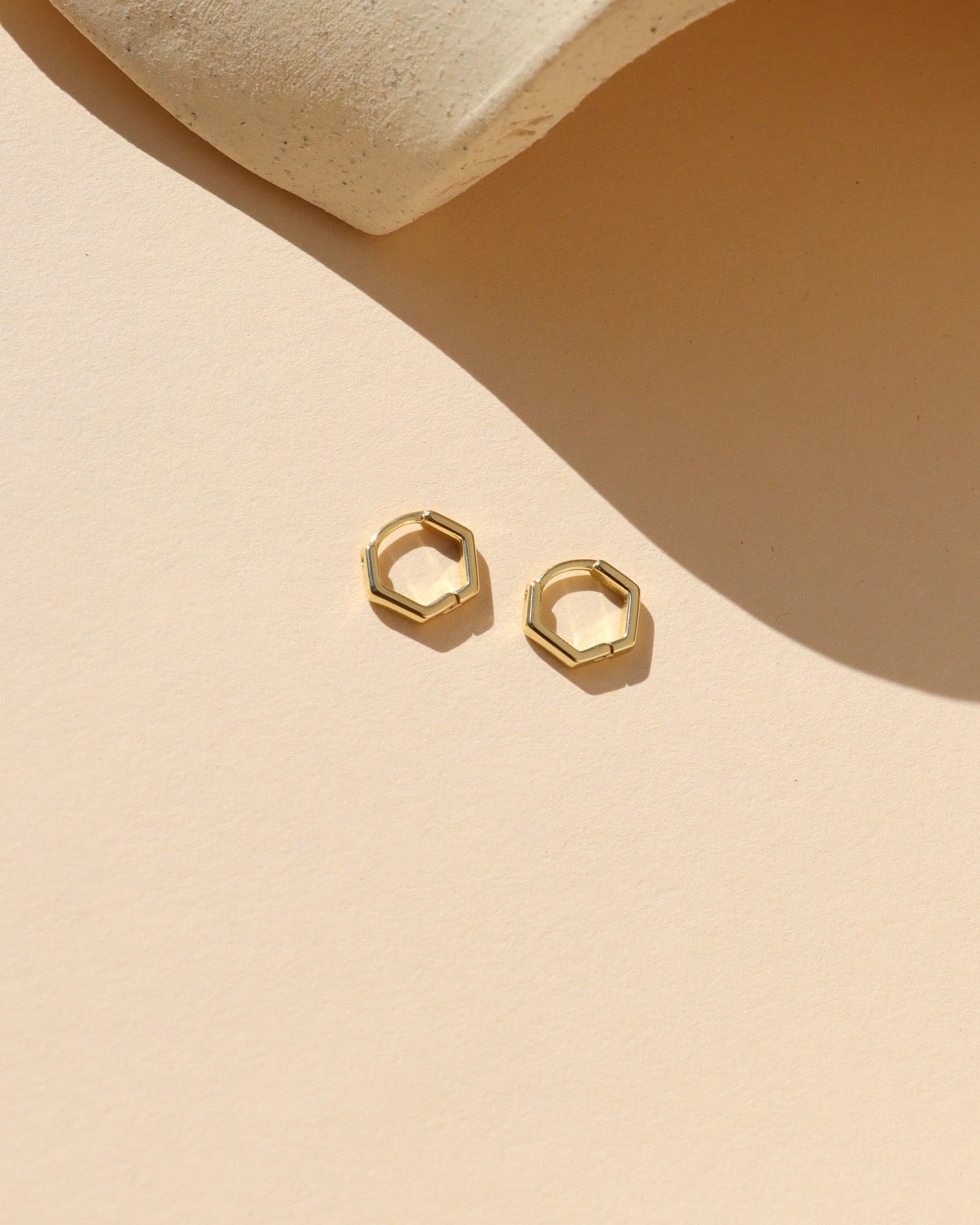 Gold hexagonal stud earrings on a beige background