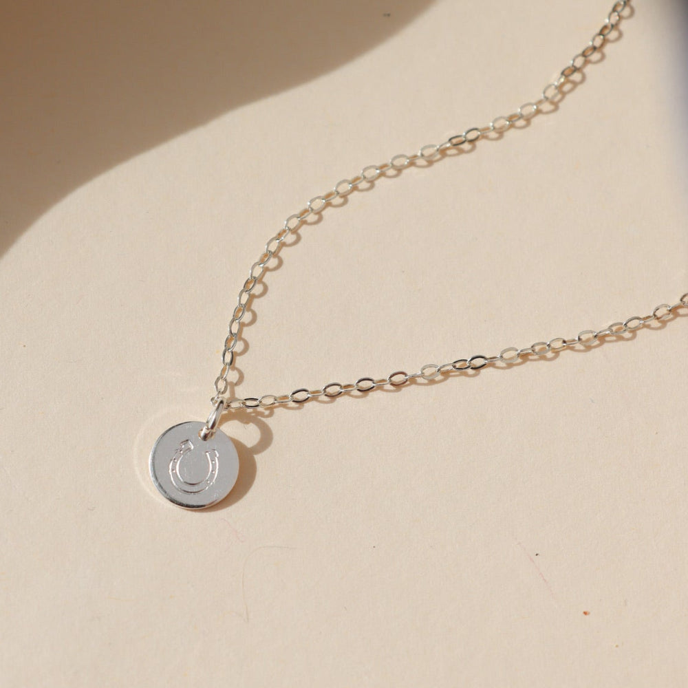 sterling silver disk with horseshoe stamp on a delicate chain necklace on a light dish