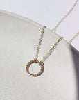 14k gold fill Spiral Necklace laid on a white plate in the sunlight. This necklace features the simple chain with the spiral eternity disc.