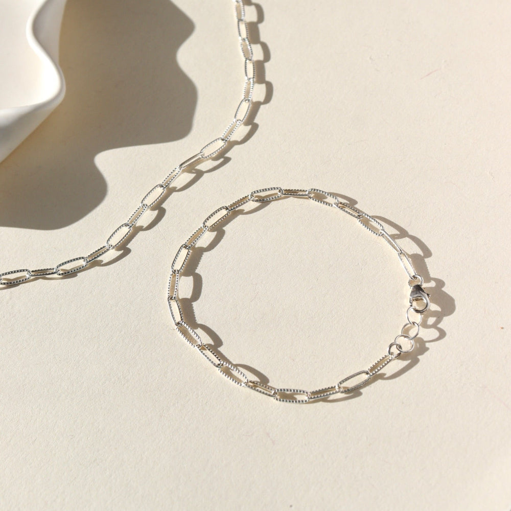 Silver chain necklace and bracelet on a beige background