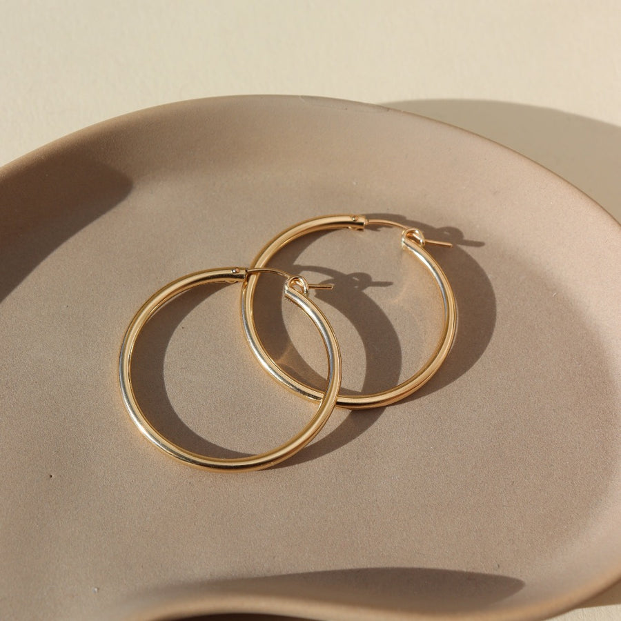 14k gold fill large classic hoop earrings for everyday, photographed on a ceramic dish