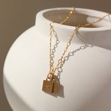 14k gold Taytum Tag Necklace laid on a white pot in the sunlight. This necklace features either the Hali chain or the Stevie chain.