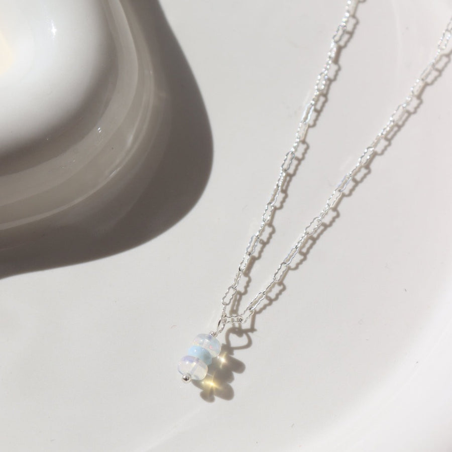 925 sterling silver Gender Reveal Necklace laid on a white plate in the sunlight. This necklace features a beautiful mini paper clip chain that is met together with either a pink or blue opal gemstones.