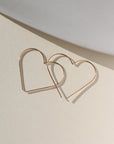 14k gold fill slide earrings in a heart shape, photographed on a sunlit backdrop