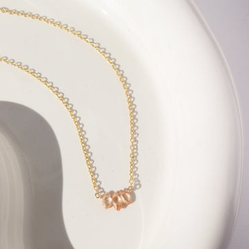 14k gold fill Gaia Necklace laid on a white plate in the sunlight. This necklace features the simple chain and is then met together by three zircon stones. 