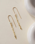 gold chain earrings featuring a small pearl on a hook-style earring, photographed on a sunlit table