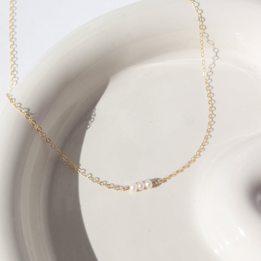three freshwater pearls lined up on a 14k gold fill simple chain, made by Token Jewelry , photographed on a white ceramic dish