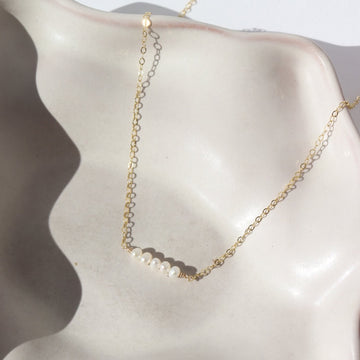 five freshwater pearls lined up on a 14k gold fill simple chain, made by Token Jewelry , photographed on a white ceramic dish