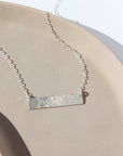 925 Sterling Silver Matriarch Necklace laid on a tan plate in the sunlight. This necklace features either the simple chain and or the April chain and the word "NANA". you can have the option of a smoother or hammered.