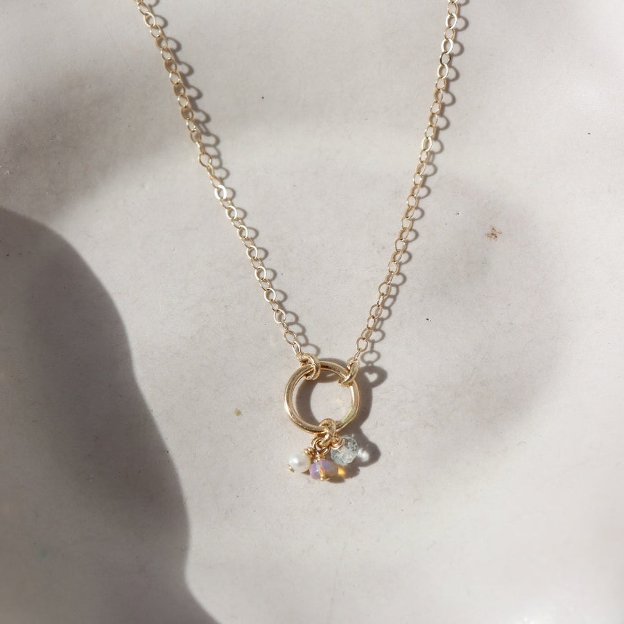 14k solid gold necklace made by Token Jewelry, featuring a simple chain and circle, with customizable birthstone charms, photographed on a white dish