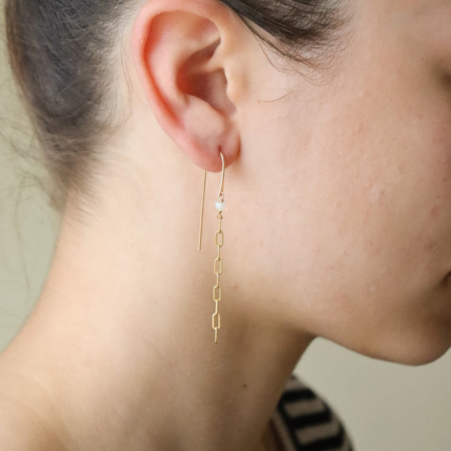 gold chain earrings featuring a small pearl on a hook-style earring, photographed on a model