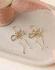 delicate 14k gold fill bow earring hand made by Token Jewelry, photographed on a ceramic dish with a light pink ribbon