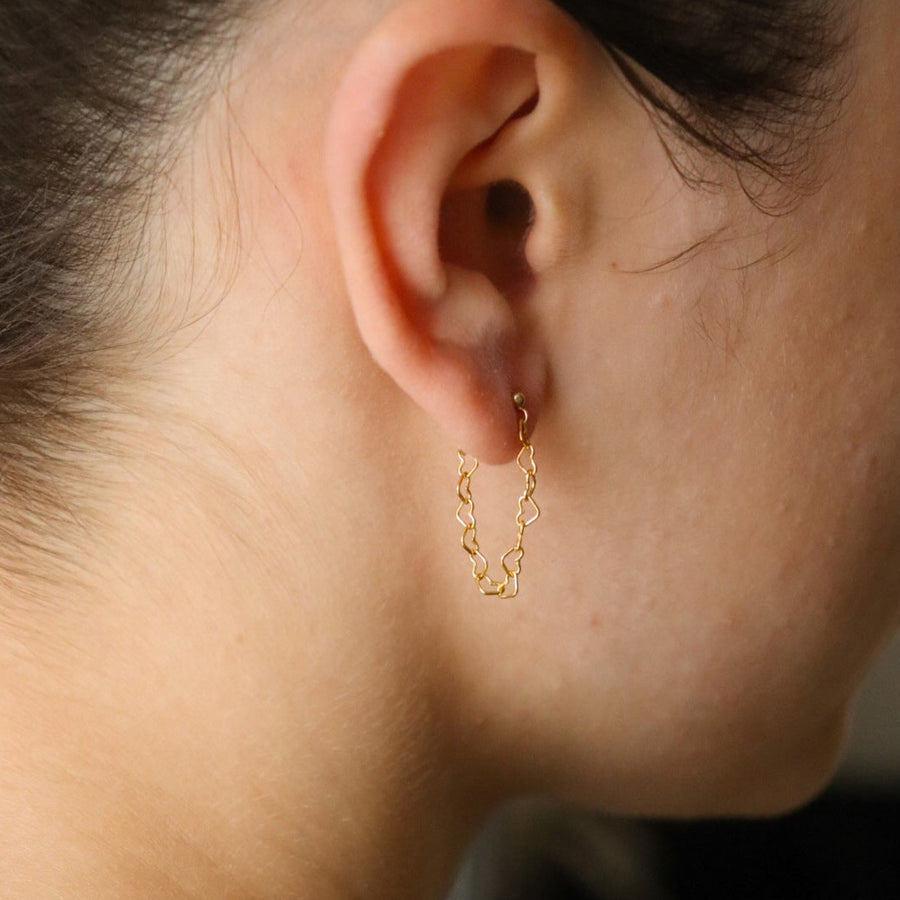 a heart chain on stud earrings, photographed on a model