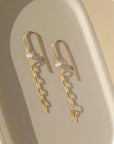 14k gold fill dangle earrings. These earrings have a gold hook that loops into your ear then a dangle tiny moonstone gemstone, followed by the narrow link chain. This earring is placed on top of a gray plate that is sitting in the sunlight. 
