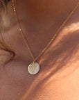 Model wearing 14k gold fill Moon drop necklace in the sunlight. This necklace features our simple chain met by a hammered coin, making it look like the moon.