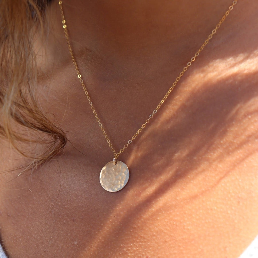 Model wearing 14k gold fill Moon drop necklace in the sunlight. This necklace features our simple chain met by a hammered coin, making it look like the moon.